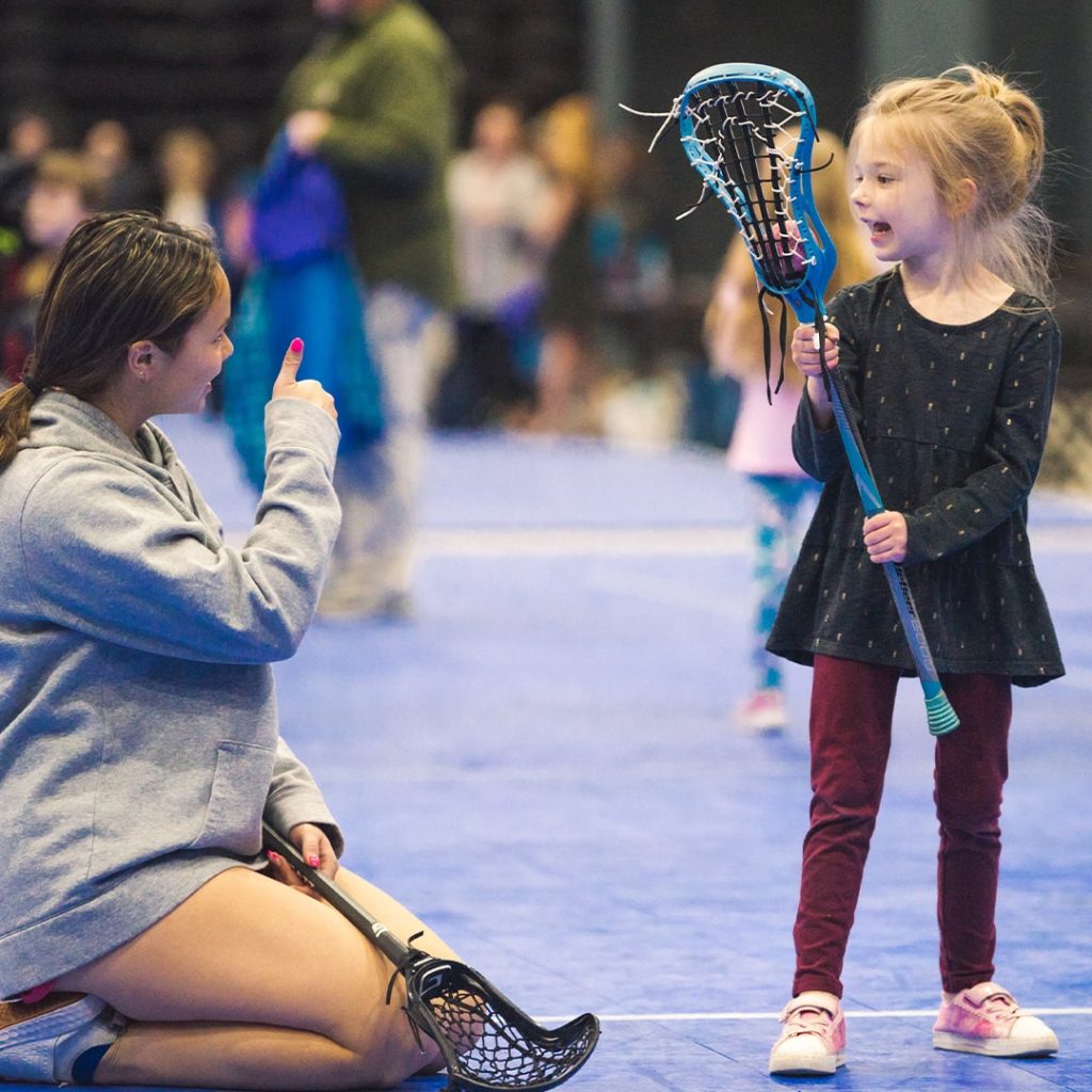 Little girl holding a lacrosse stick and a teenager giving a thumbs up