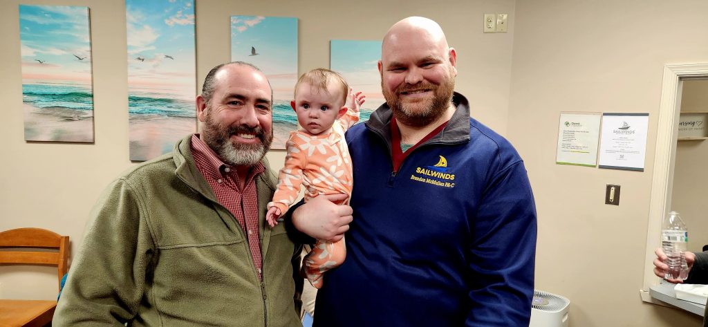 Father holding a baby beside a grown man with a beard