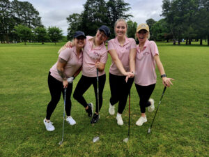 Group of 4 women wearing pink shirts holding golf clubs