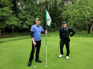 Man holding a golf flag standing next to a person in black holding a golf club