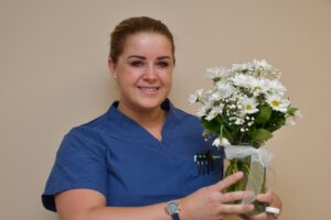 Headshot of a female nurse in scrubs holding flowers