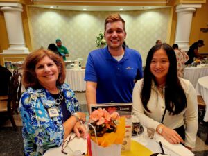 Group of three people smiling; standing at a table