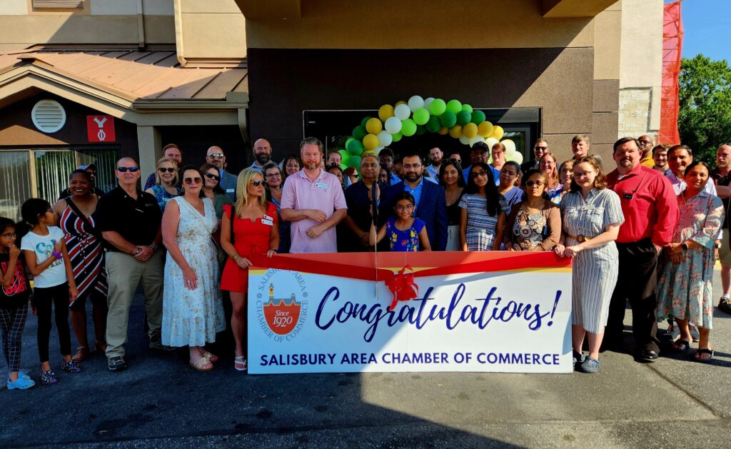 Large group of people holding a banner for a ribbon cutting