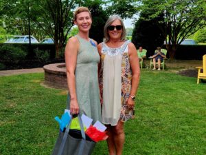woman in a green dress holding a gift bag standing with a woman in a floral dress outdoors