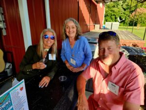 Woman in black shirt, woman in blue shirt and man in a pink button down shirt sitting outside