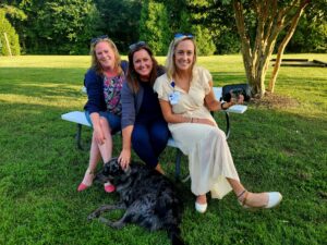 Group of three women with a dog sitting on a bench beside a tree