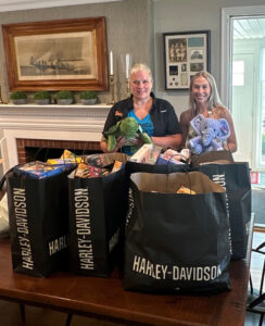 Two women with several bags full of donations from Rommel Harley-Davidson