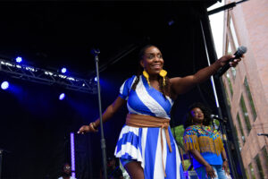 Woman in a stripped dress on stage waving to the crowd