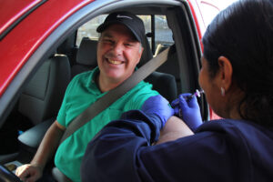 Man sitting in his car getting a flu shot by a nurse through the car window