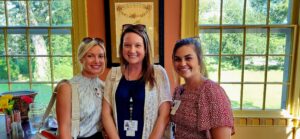 3 woman smiling at a ribbon cutting.