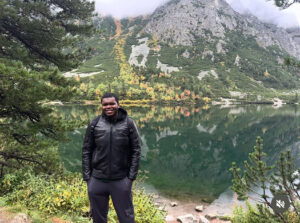 A man standing for his picture in front of a lake.
