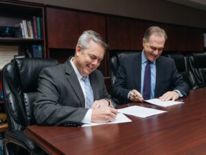 Two men signing papers at a desk.