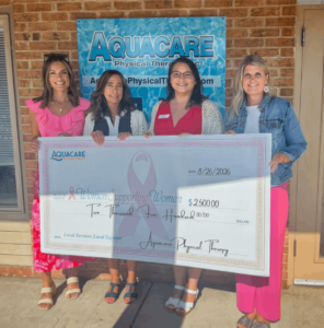 aquacare-check-presentation Four women standing outside in front of an Aquacare banner, presenting a large donation check of $2,500 to Women Supporting Women.