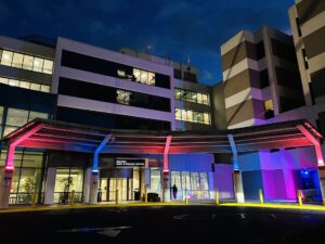 Nighttime exterior view of the Guerrieri Heart & Vascular Institute building entrance illuminated with red, white, and blue lights along the covered canopy overhang.